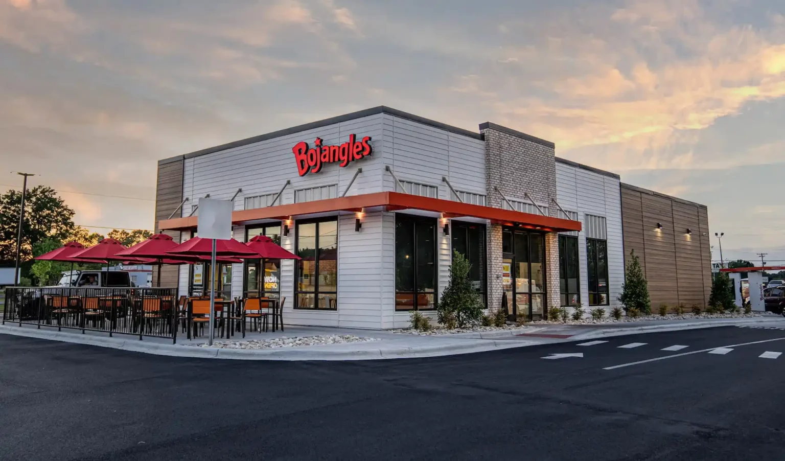 Exterior view of a Bojangles restaurant with outdoor seating and red umbrellas.
